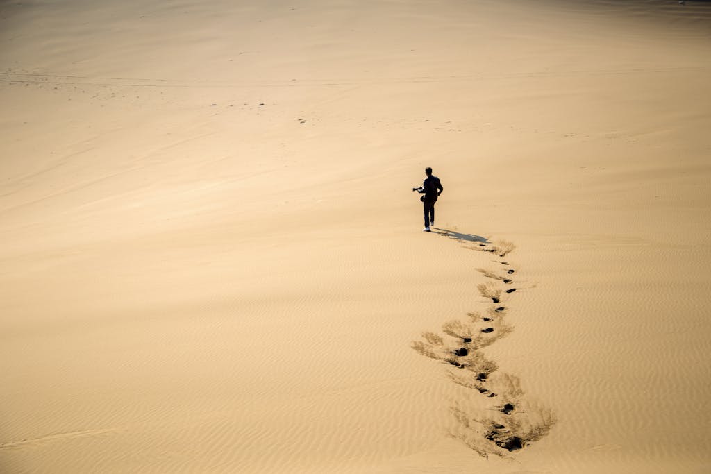 A photographer walking across vast sand dunes in the Iranian desert, leaving footprints behind.