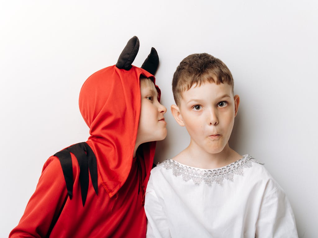 Two children dressed as an angel and a devil, displaying playful expressions against a white background.