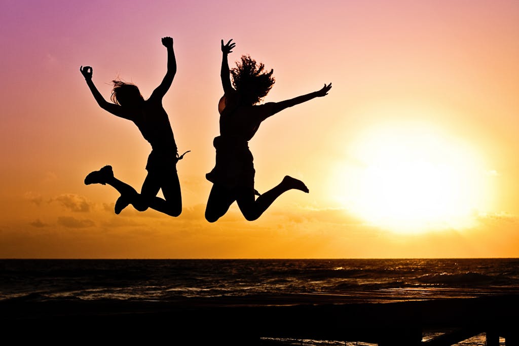 Silhouettes of two people joyfully jumping on a beach during a vibrant sunset.